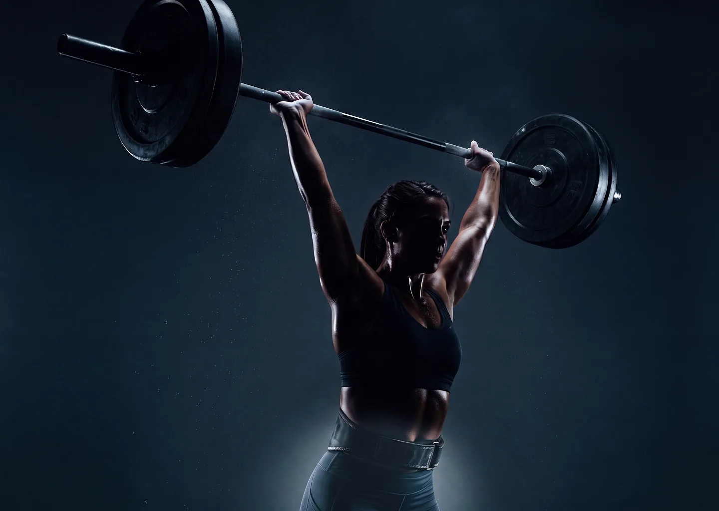 Athlete holding a loaded barbell overhead in a dark gym